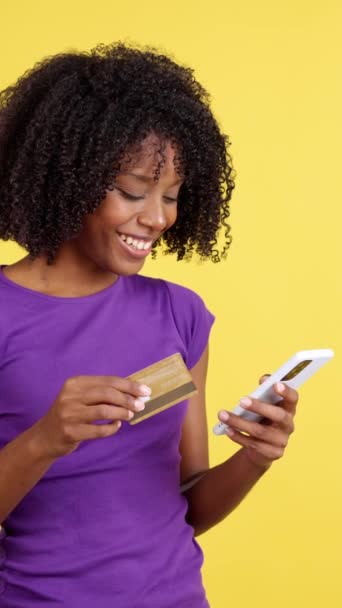 モバイルと黄色の背景を持つスタジオでクレジットカードでオンラインアフロヘアショッピングを持つ女性 — ストック動画