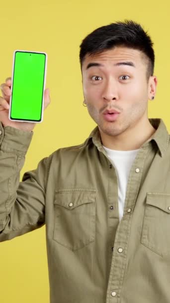 黄色の背景を持つスタジオで緑の画面を持つモバイルを保持している中国の男 — ストック動画