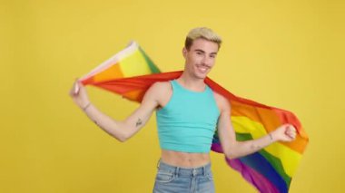 Stüdyoda sarı arka planda lgbt bayrağıyla sarılı mutlu gay adam.