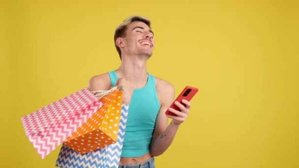 快乐的基佬一边用手机一边在有黄色背景的工作室里翻翻购物袋 — 图库视频影像
