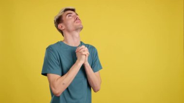 Eşcinsel adam elleri bağlı dua ediyor, sarı arka planla stüdyoya bakıyor.