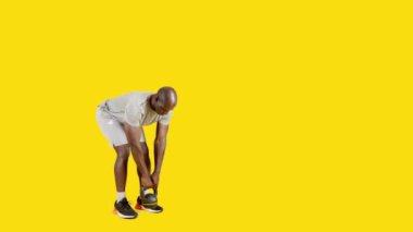 Stüdyoda spor elbiseli bir Afrikalı 'nın sarı arka planlı videosu var. Kettlebell ile ölü kaldırıyor.