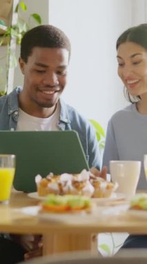 Evde dizüstü bilgisayar kullanarak kahvaltı yapan mutlu bir çiftin yavaş çekim videosu.