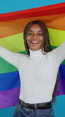 Gökkuşağı lgbt bayrağı sallayan gülümseyen Afrikalı bir kadının mavi arka planına sahip bir video.