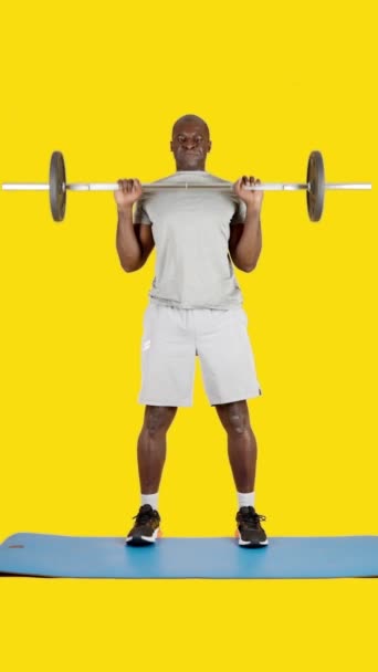 ビデオでスタジオで黄色の背景のスポーツアフリカ人男性重量挙げクリーンとともにバー — ストック動画