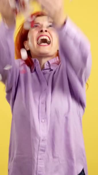 Szczęśliwa Ruda Dojrzała Kobieta Otoczona Konfetti Latające Powietrzu Studio Żółtym — Wideo stockowe