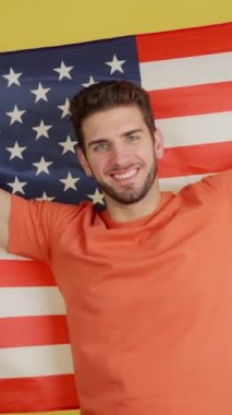 Stüdyoda sarı arka planda Kuzey Amerika bayrağını dalgalandıran mutlu beyaz adam.