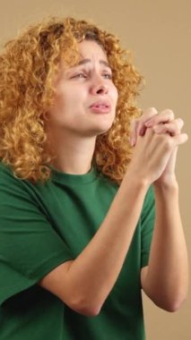 Studio video of a woman with curly hair looking up while praying with folded hands