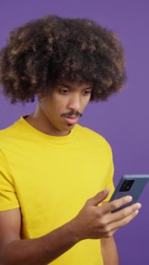 Surprised african man with curly hair looking the screen of a mobile in studio