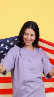 Stüdyoda sarı arka planda Kuzey Amerika bayrağı taşıyan mutlu beyaz kadın.
