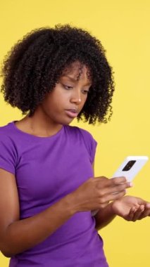 Sinirli ve şüpheci bir ifadeyle telefona bakan Afrikalı bir kadının sarı arka planlı videosu.