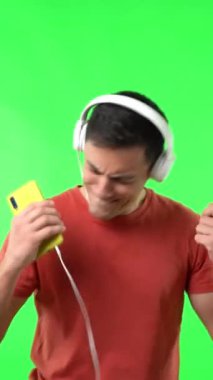 Kırmızı tişörtlü yalnız bir adam kulaklıktan müzik dinlerken mutlu bir şekilde dans ediyor.