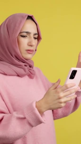 Беспокойная Мусульманка Пользуется Мобильным Телефоном Студии Жёлтым Фоном — стоковое видео