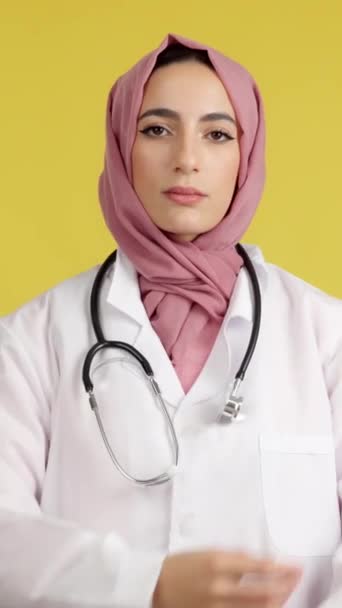 严肃的女性穆斯林医生 手挽手交叉看着黄色背景的工作室里的相机 — 图库视频影像