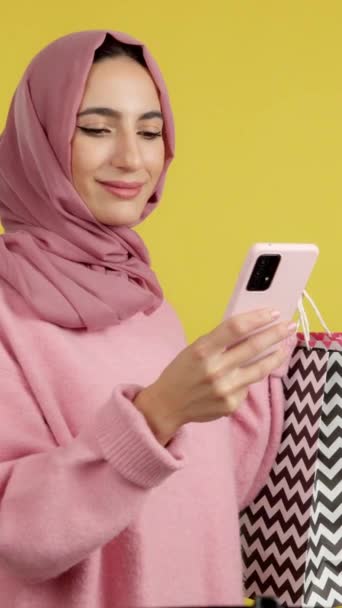 Muszlim Használja Mobilt Miközben Bevásárlószatyrokat Rejteget Sárga Háttér — Stock videók