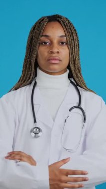 Video with blue background of a serious african female doctor with arms crossed looking at camera