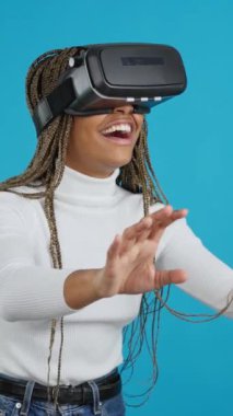 Video with blue background of a smiling african woman gesturing with hands while using a virtual goggles