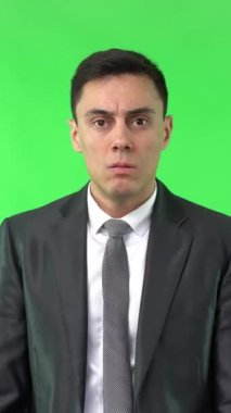 Zarif takım elbiseli, ağzı eliyle kapatan ve stüdyoda krom anahtarla tek başına dikilirken kameraya bakan endişeli bir erkek.