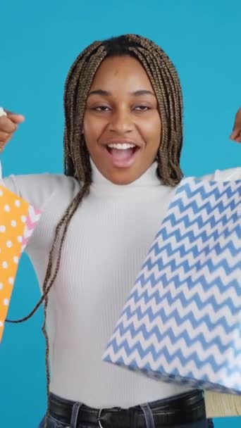 笑顔のアフリカの女性の青い背景を持つビデオ喜んでショッピングバッグを運ぶ — ストック動画