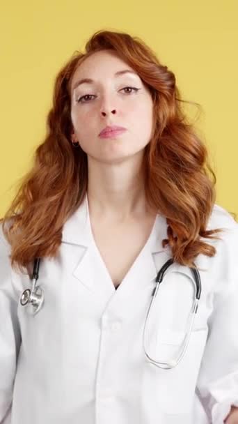 严重红头发的女医生 手臂交叉在黄底工作室里 — 图库视频影像
