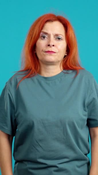 在蓝色背景的演播室里 成熟的红头发女人看着带着忧郁表情的相机 — 图库视频影像