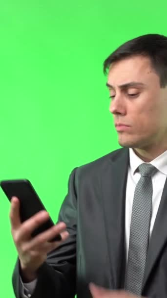 ポジティブな男性でエレガントなスーツでビデオを見ます携帯電話上の笑顔とともに立って絶縁オンクロマキーライトスタジオ — ストック動画
