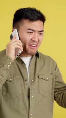 Angry chinese man talking to the mobile in studio with yellow background