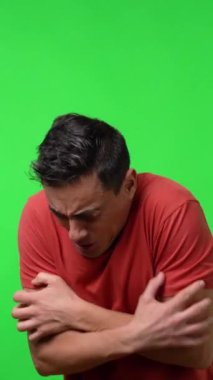 Çok soğuk bir adam ısınmak için kendine sarılıyor. Kırmızı gömlekli. Orta boy. Krom yeşil arkaplan.