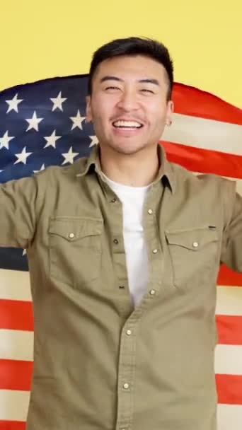 Szczęśliwy Chińczyk Patrzący Kamerę Owijający Flagą Ameryki Północnej Studio Żółtym — Wideo stockowe