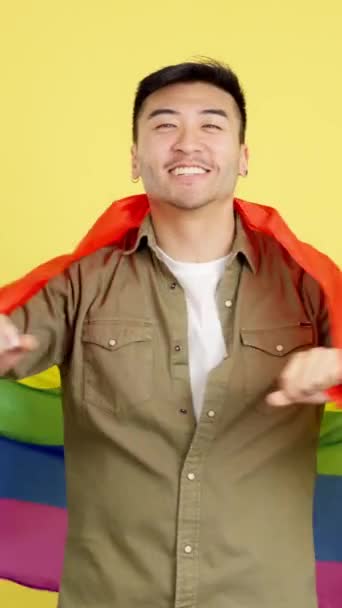 Happy Chinese Man Wrapping Lgbt Rainbow Flag Studio Yellow Background — Stock Video