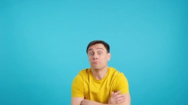 Stüdyoda mavi arka planı olan bir adam gülümseyerek başını sallıyor.