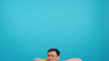 Stüdyoda mavi arka planı olan bir adam gülümserken yukarı çıkıp işaret ediyor.