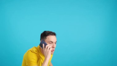 Stüdyoda cep telefonuyla konuşurken elini kaldıran bir adamın mavi arkaplanlı videosu. Çerçeve boş başlar, adam aşağıdan görünür ve altta kaybolur..