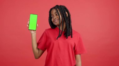 Stüdyoda kırmızı arka planda krom ekranlı cep telefonu tutan mutlu Afrikalı kadın.