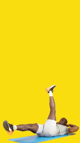 ビデオでスタジオで黄色の背景のアフリカ人男ありますScissor Crunches上のマット — ストック動画
