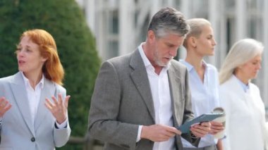 Yetişkin bir iş adamının dışarıda iş arkadaşlarıyla yürürken tablet kullanmasının yavaş çekim videosu.