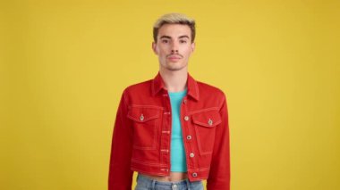 Renkli elbiseli eşcinsel stüdyoda sarı arka planda kameraya bakıyor.