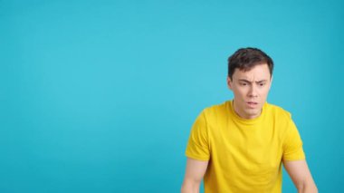 Stüdyoda korku içinde el kol hareketi yapan ve yana bakan korkmuş bir adamın mavi arka planlı videosu var.