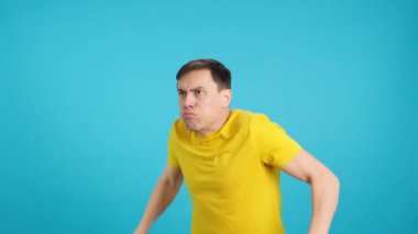 Stüdyoda vücut geliştirme pozları veren bir adamın mavi arka planlı videosu.