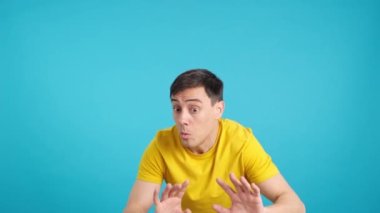 Stüdyoda mavi arka planı olan bir adam, kameraya ve diğerlerine sessizlik çağrısı yapıyor.