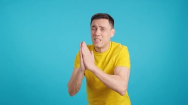 Stüdyoda mavi arka planı olan, el ele tutuşup kameraya bakan umutsuz bir adamın videosu.