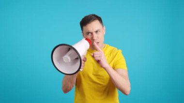 Stüdyoda, izleyicilere megafonla konuşan bir liderin mavi arkaplanlı videosu var.