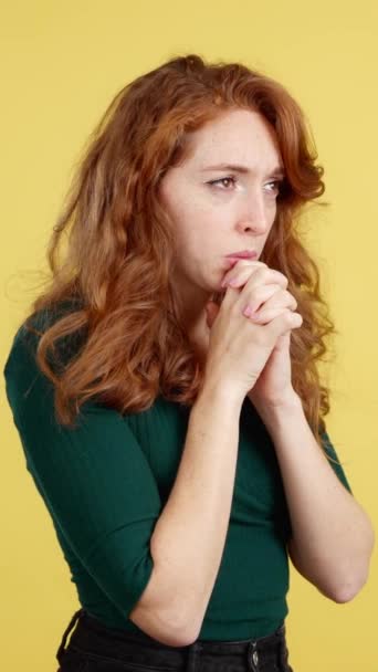 赤毛女性見上げながら祈りますともに折り畳まれた手でスタジオとともに黄色の背景 — ストック動画