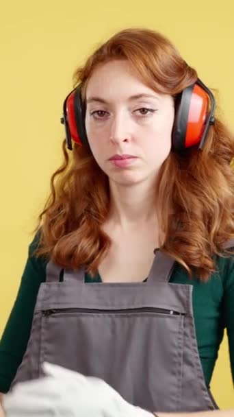 严肃的红头发女工手挽手站在一边 看着黄色背景的工作室里的摄像机 — 图库视频影像