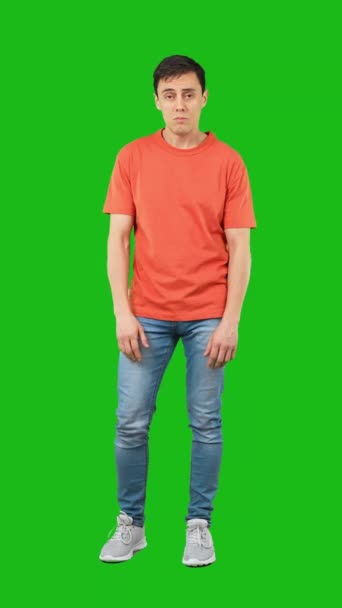 フル長いです怖いです男性でジーンズとオレンジTシャツカメラを見て 驚くほど後ろから危険から隔離された緑の背景 — ストック動画