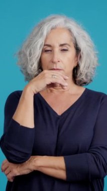 Studio video with blue background of an aged woman gesturing and looking up with thoughtful expression