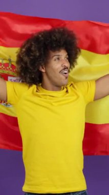 Happy african man with curly hair raising a spanish national flag in studio