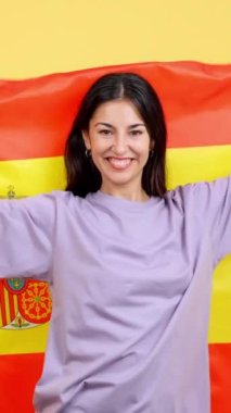Happy caucasian woman smiling and raising a spanish national flag in studio with yellow background