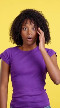 Cool woman with afro hair expressing surprise in studio with yellow background