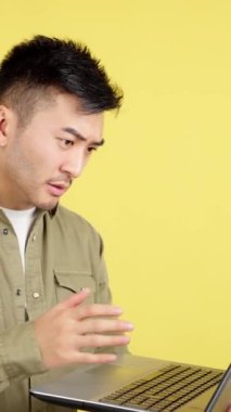 Chinese man having a problem with a laptop in studio with yellow background